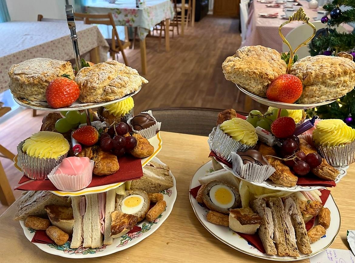 Two tiered stands of afternoon tea: scones topped with strawberries, little cakes, sandwiches and halved scotch eggs